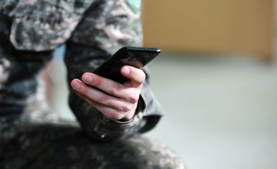 Photo of a person wearing camouflage and holding a smartphone