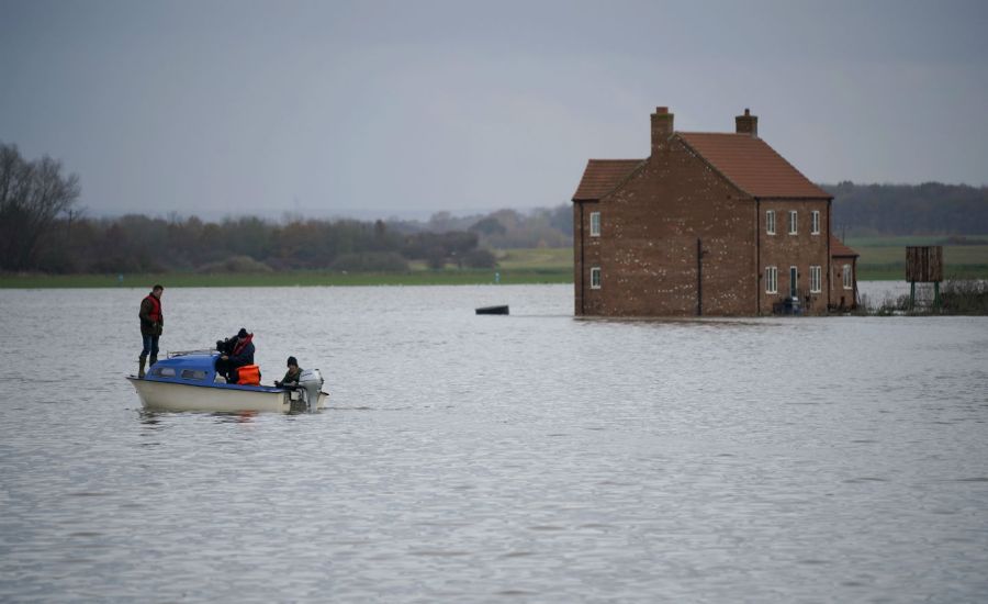 Photo of people on a boat looking at a house in floodwaters