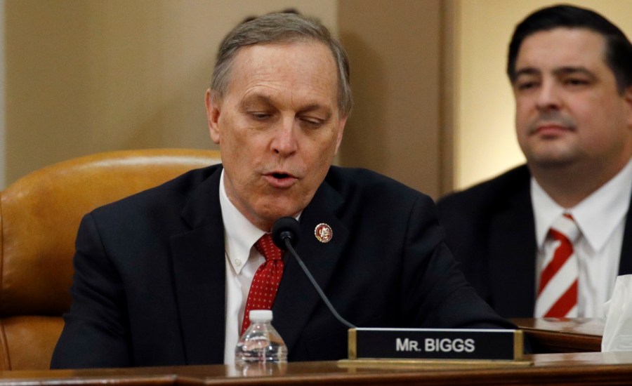 Arizona representative andy biggs sits in front of a podium and speaks into a mic