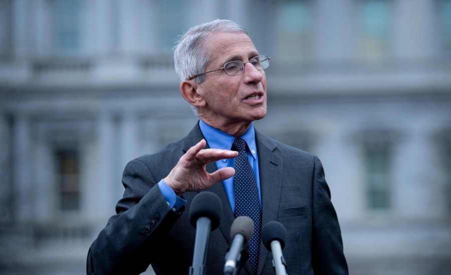 dr anthony fauci stands in front of mics at a podium