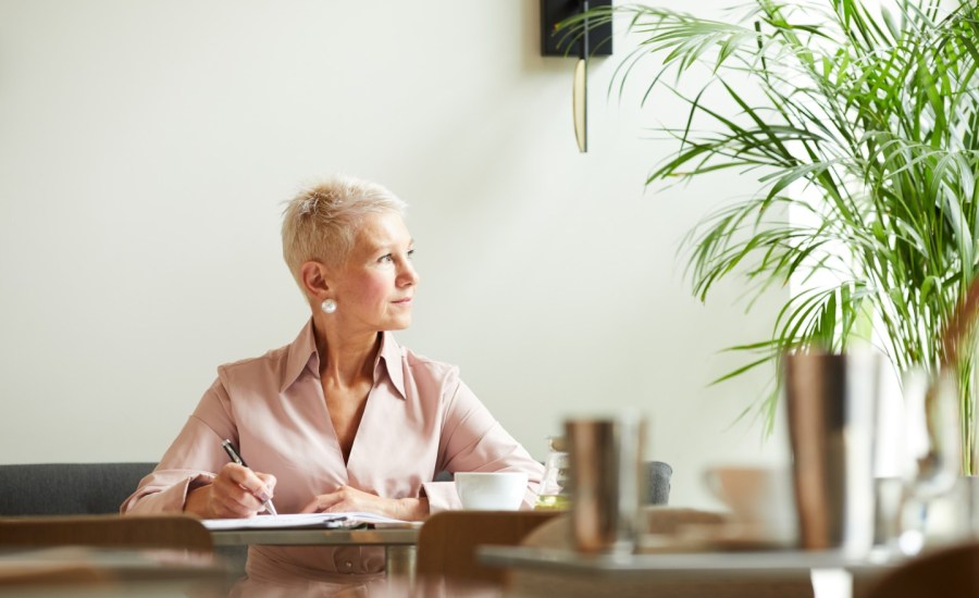 an older businesswoman looks out the window while sitting at a table