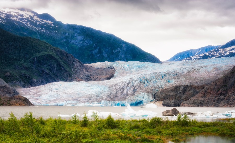 Mendenhall Glaier under cloudy skies in Tongass National Forest in Alaska. Proglacial lake with chunks of ice floating on it's surface forms at the glacier's base