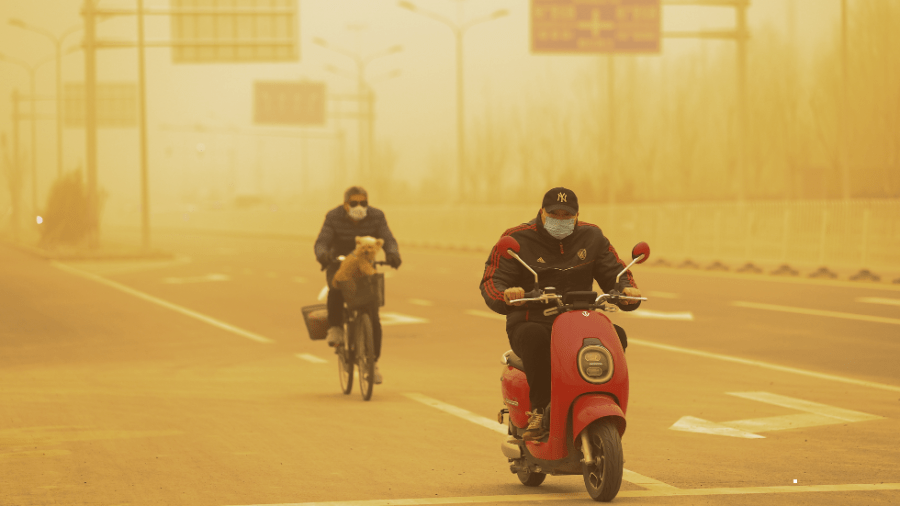 People wearing protective masks ride their bikes during a sandstorm in Beijing