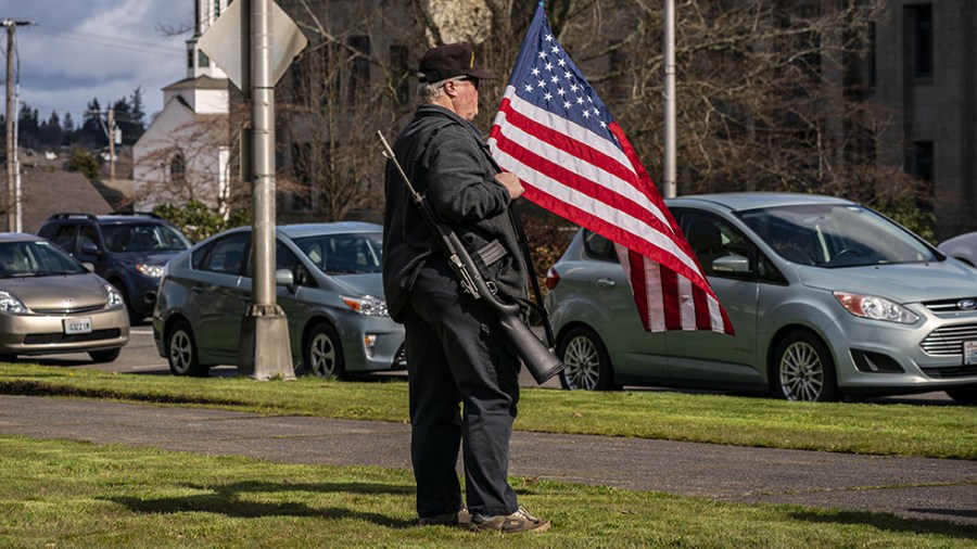 A man holds a flag and a gun at a Second Amendment rally