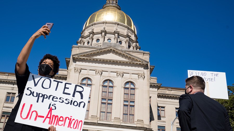 A woman holds a sign at a protest over the new voting restrictions law in front of Georgia Capitol building