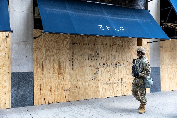 A member of the National Guard walks past a boarded up store front as he patrol downtown Minneapolis