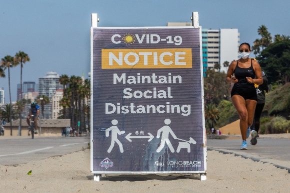 A woman wearing a facemask jogs near a notice about maintaining social distance