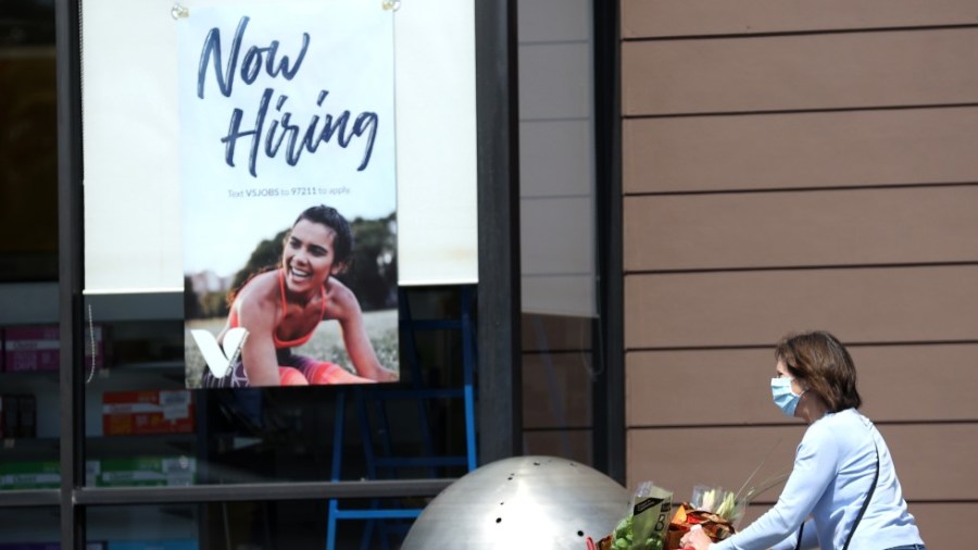 A woman walks by a sign that says "now hiring"