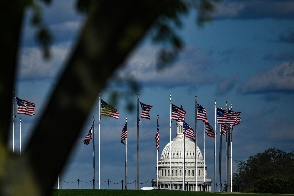 The dome of the US Capitol building is seen behind a row of US flags 