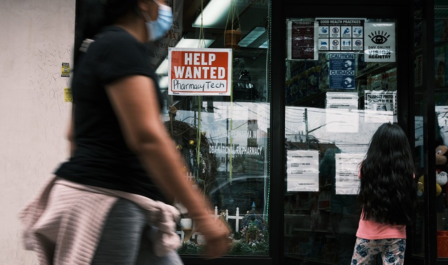 A person in a mask walks past a hiring sign in New York