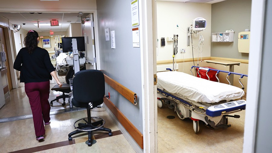 An empty bed with white sheets is seen in the Emergency Department at Providence St. Mary Medical Center as a staff member walks by