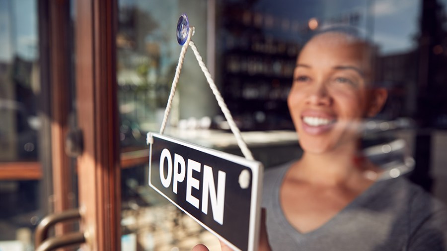 A Black woman business owner flips an "Open" sign on her store window