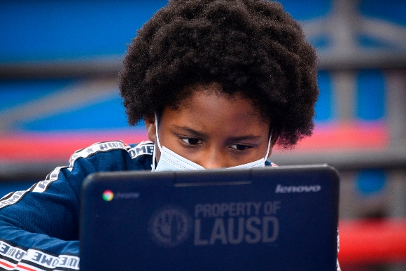 A child wears a face mask as they attend an online class at a learning hub inside the Crenshaw Family YMCA