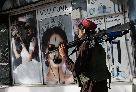 A Taliban fighter walks past a beauty salon with images of women defaced using spray paint