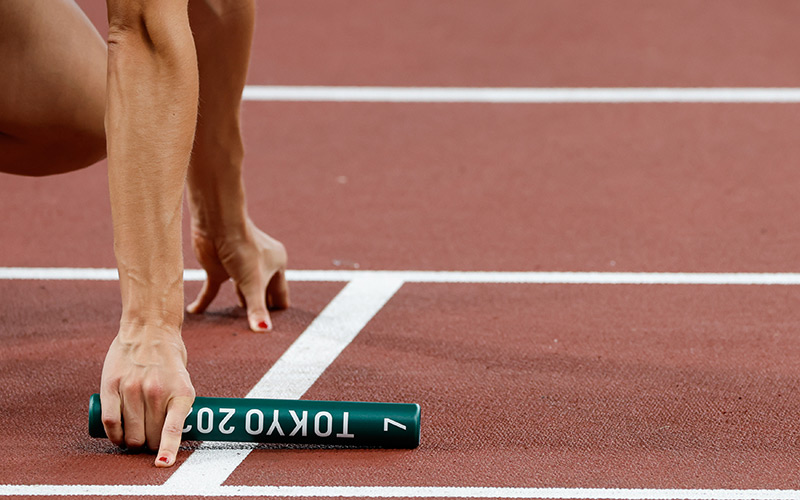 A Team Switzerland runner readies herself at the starting line with a green "Tokyo 2020" baton