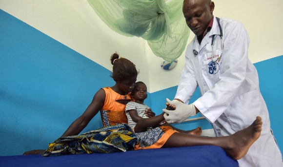 A woman holds a child who has contracted Malaria and is examined by a doctor