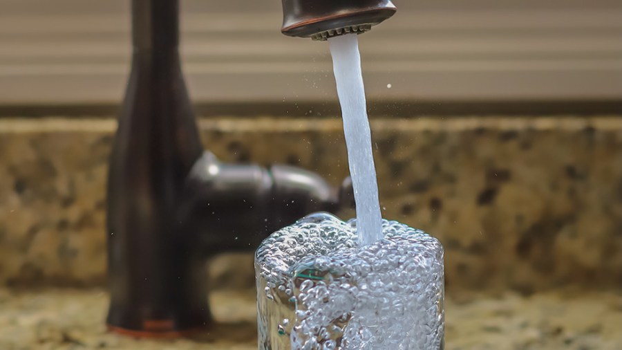 Water coming out of a kitchen faucet into a glass cup