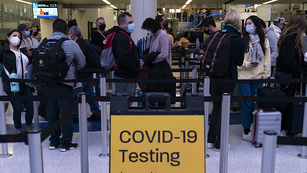 Travelers wait in line for screening near a sign for a COVID-19 testing site at the Los Angeles International Airport in Los Angeles, Calif., on  Wednesday, Nov. 24, 2021.