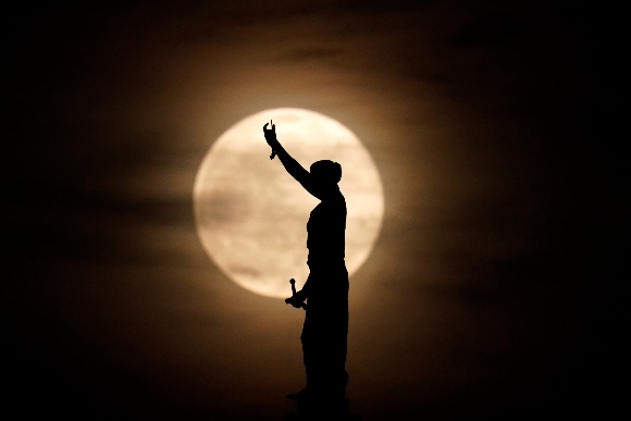 A statue of Lady Justice on top of the Polk County Courthouse is silhouetted against the rising full moon