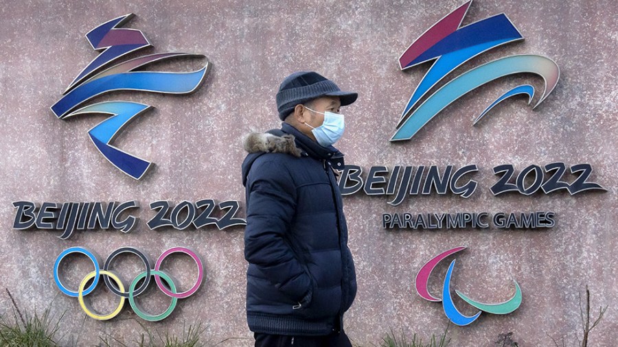 A masked man walks in front of signs for the 2022 Beijing Olympics and Paralympics