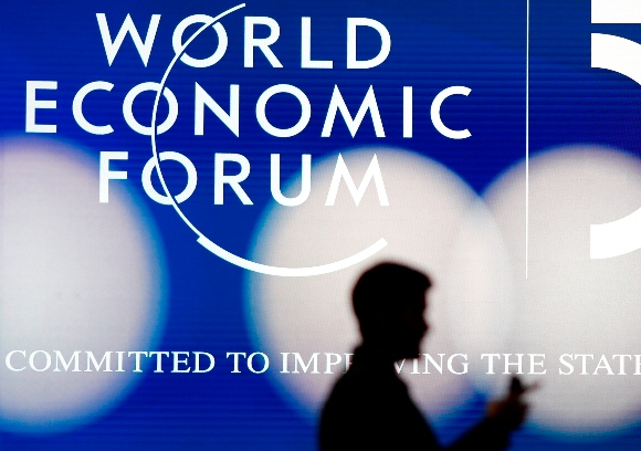 A man silhouettes in front of the logo of the World Economic Forum in Davos, Switzerland