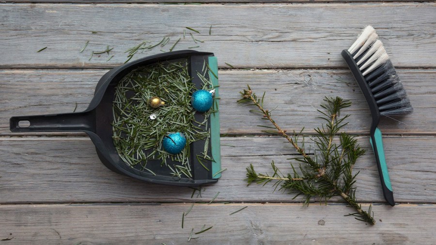 A handbroom and a dustpan filled with pine needles and 3 holidays ornaments