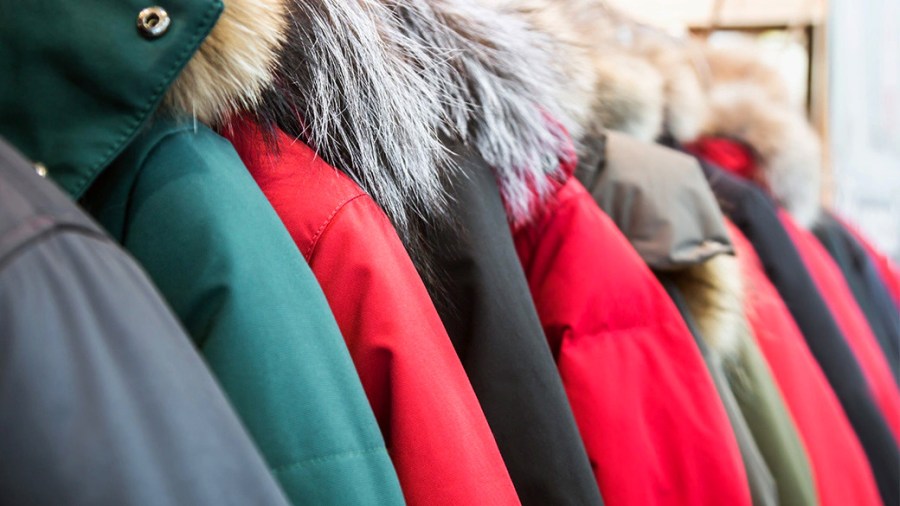 Several winter coats with hoods in different colors hanging on a rack