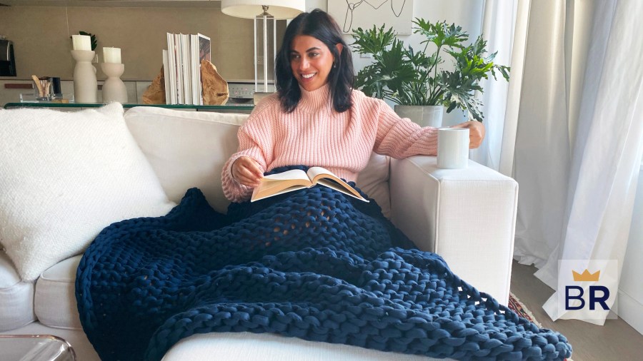 Woman under a blue Bearaby blanket reading a book