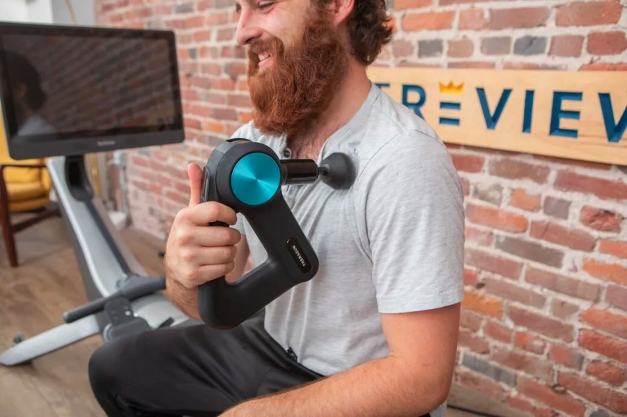 Man with red hair and beard using a Theragun on his chest