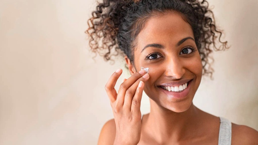 Woman with lovely dark skin applying creamy moisturizer