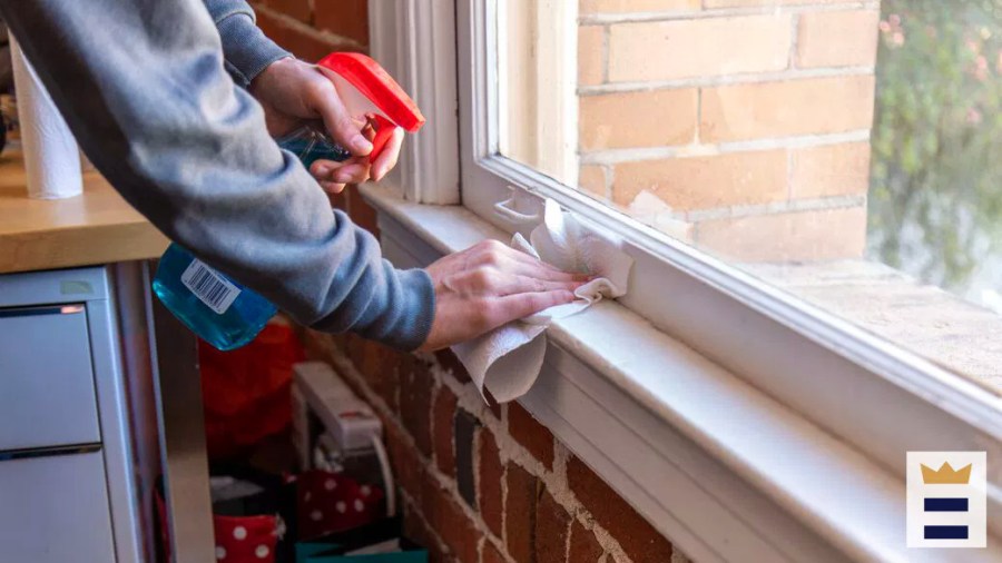 Person cleaning a windowsill with a cleaning product