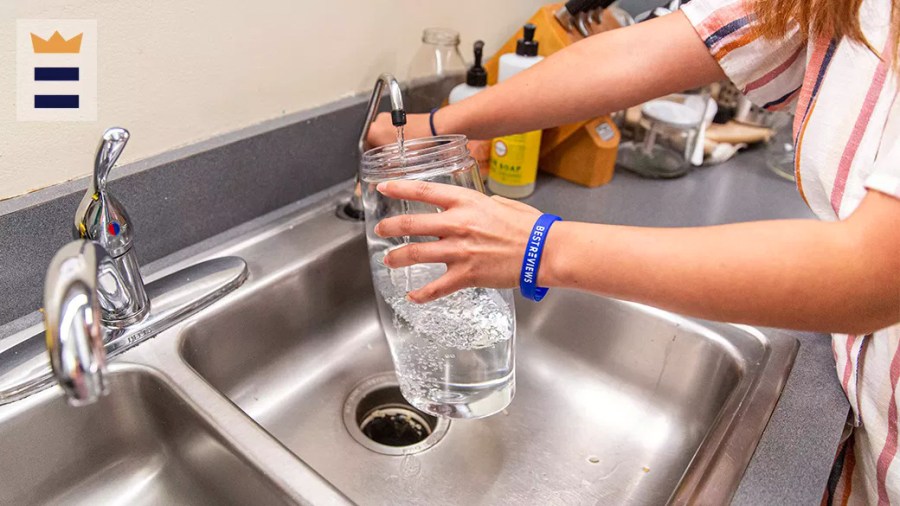 Person filling a glass jar with water at a kitchen sink