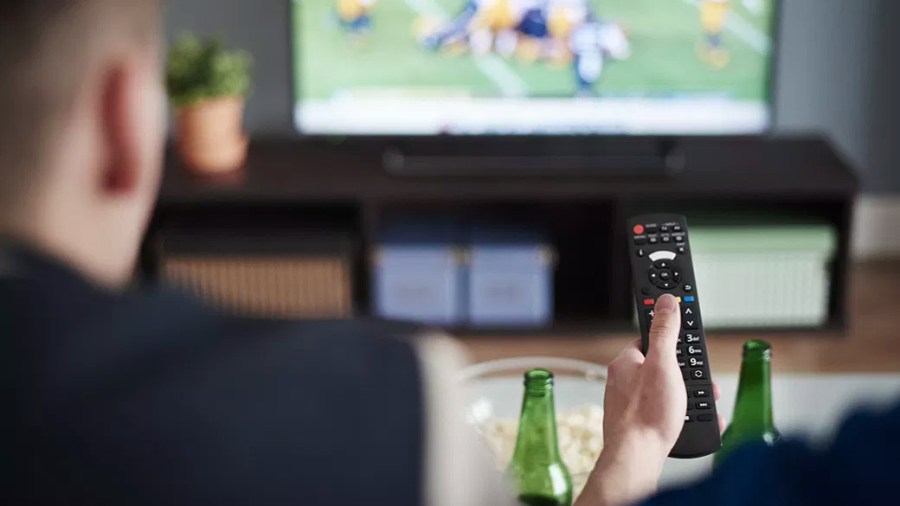 Two people enjoying food and drinks while watching a football game on a big screen TV