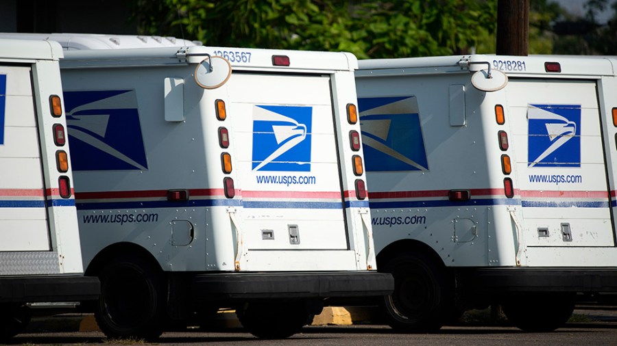 Mail trucks are parked in a Postal Service lot