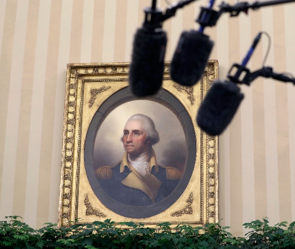 A portrait of George Washington and media microphones are seen in the Oval Office