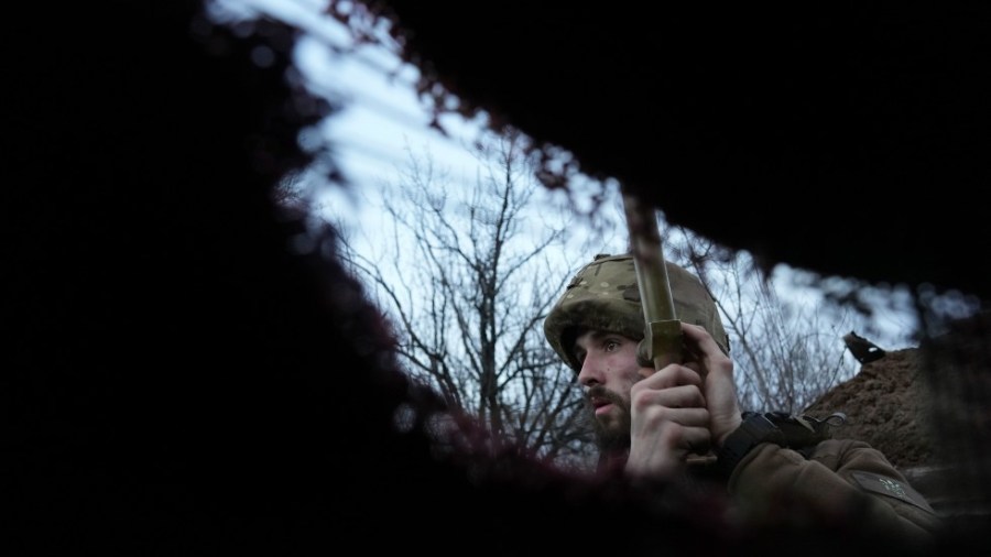 A Ukrainian service member listens to artillery shots standing in a trench