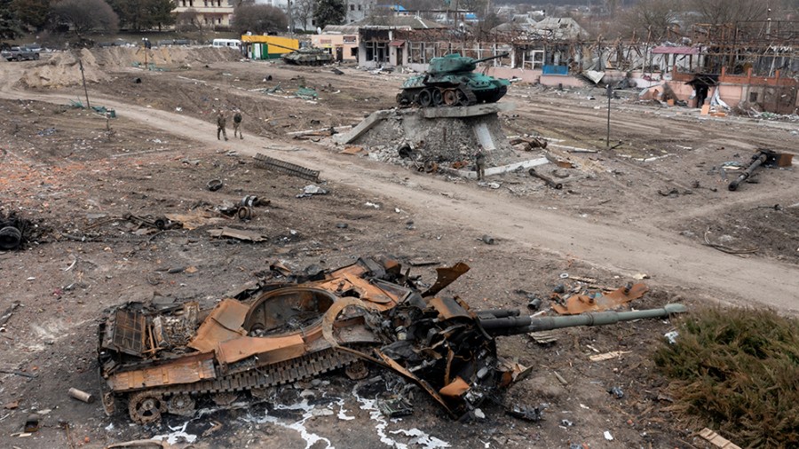 Residents pass a rust-colored damaged Russian tank in the town of Trostsyanets