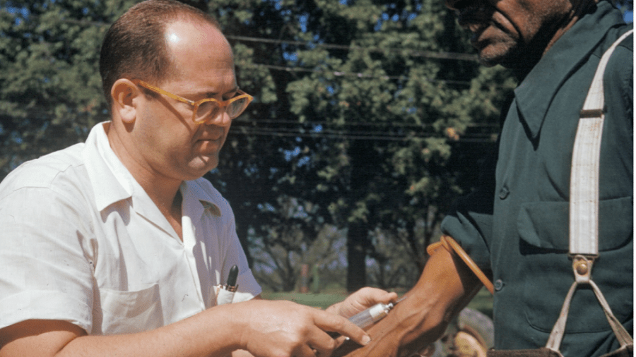 A doctor draws blood from a Black man's arm during the Tuskegee Syphilis Studyegee S