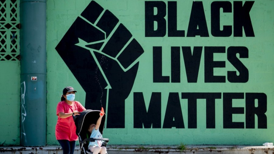 A girl in a stroller plays with a squirt gun as a woman pushes her past a Black Lives Matter mural in the Shaw neighborhood in Washington