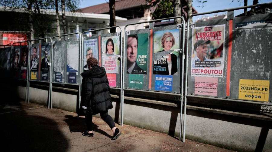 A woman walks past presidential campaign posters during the first round of the French presidential election in Saint-Denis, outside Paris