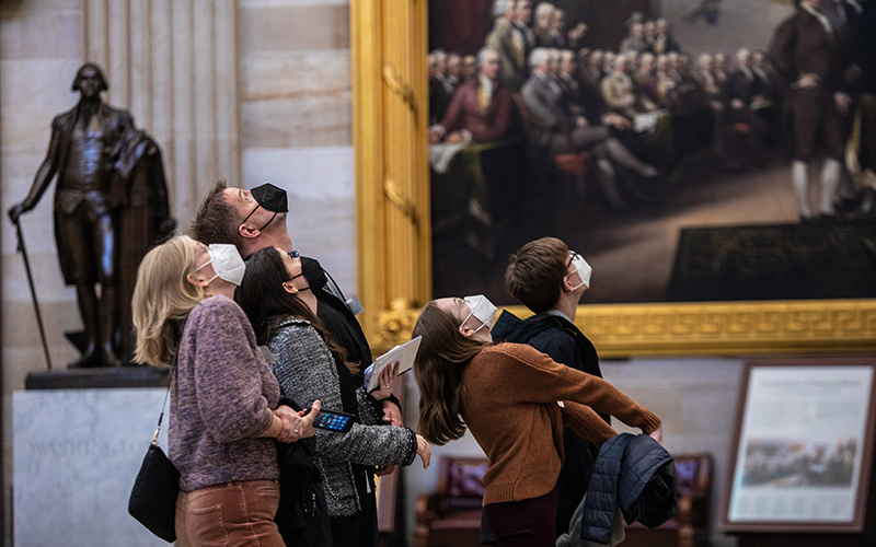 A small tour group looks up at the Apotheosis of Washington with other paintings and a statue in the background