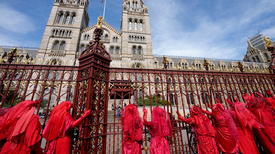 Red robed climate demonstrators perform outside the red fence of the Natural History Museum