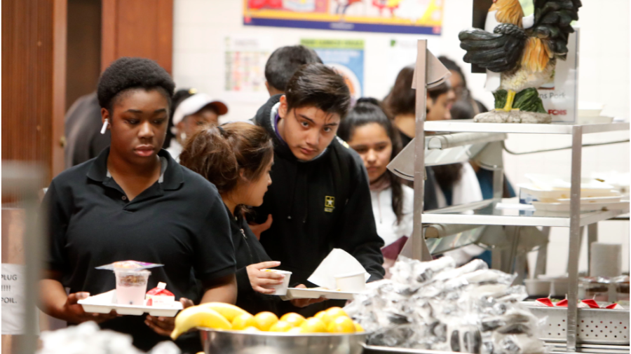 Students in black shirts stand in line holding lunch trays