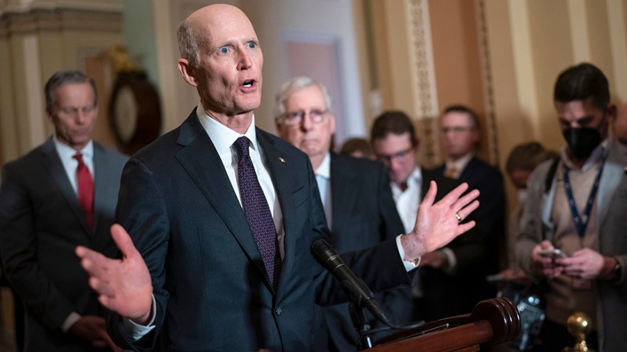 Rick Scott gestures while speaking at a microphone