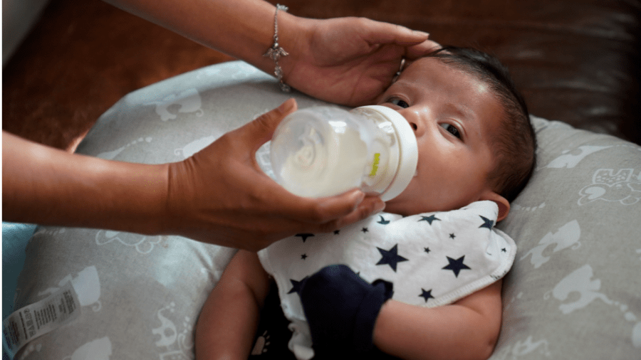 A baby wearing a white bib with blue stars being fed by a bottle.