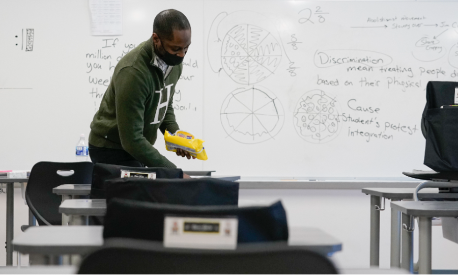 A teacher clears off a desk in front of his whiteboard.