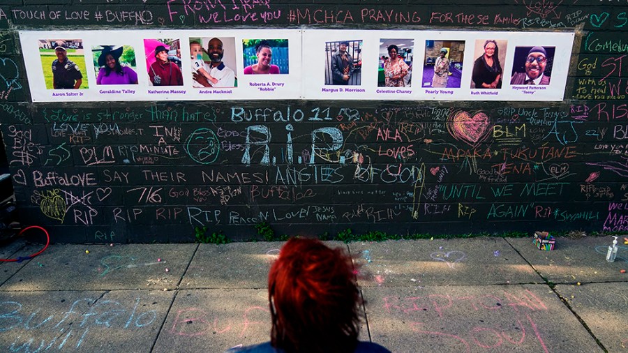 A person visits a makeshift memorial written in chalk with photos strung on a blackboard