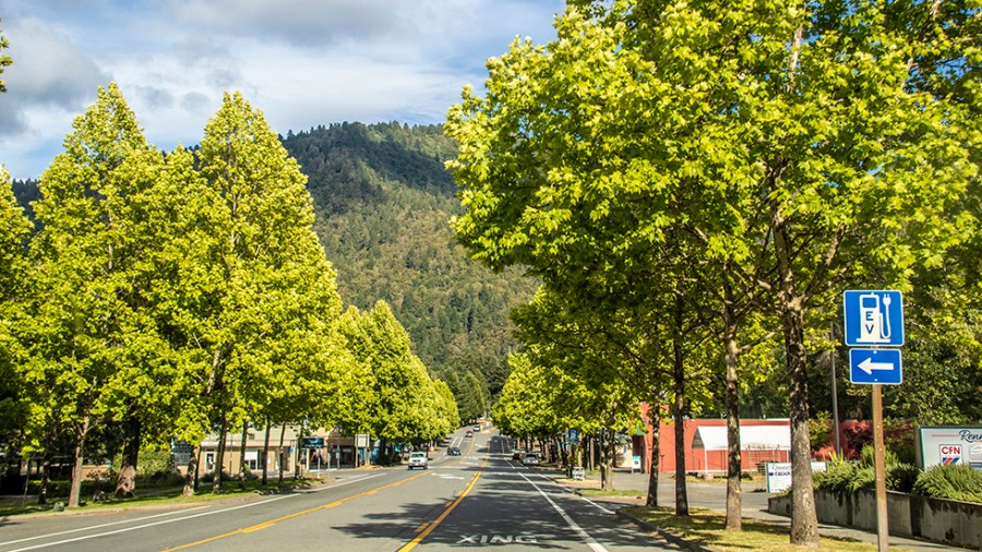 A highway is seen through small mountain town with a sign for electric car charge in Willow Creek, Calif., on May 27, 2021.