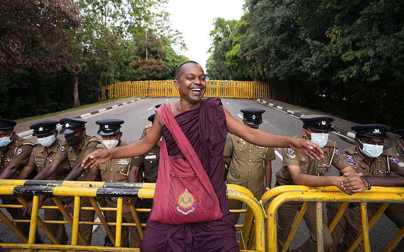 A Sri Lankan Buddhist monk smiles as he sits on a police barricade