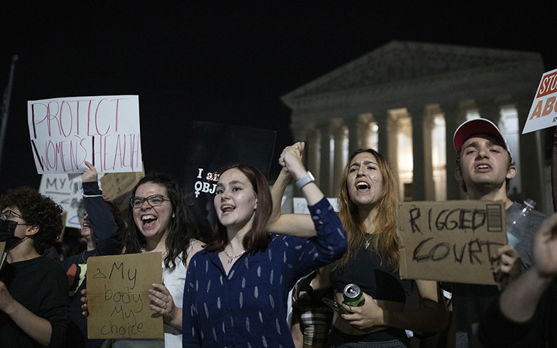 Protestors with signs reading "My body my choice" and "Rigged court" with the Supreme Court in the background at night